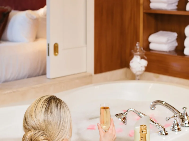 Luxury soaking bath with champagne, petals, and warm wood-toned interiors