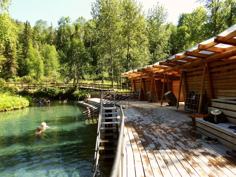 Sunny outdoor hot spring pool with deck seating and forest backdrop
