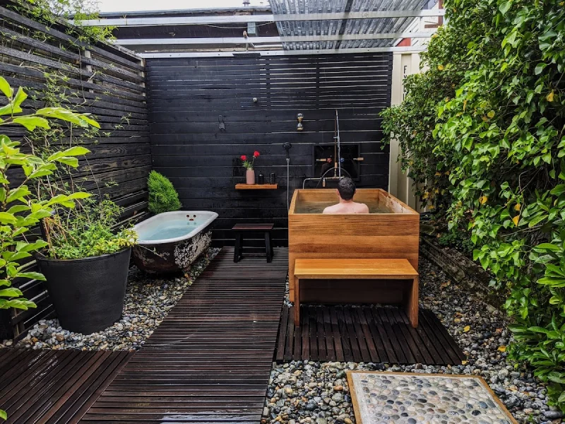 Lush private bathing courtyard with wooden tub, stone basin, and dense greenery