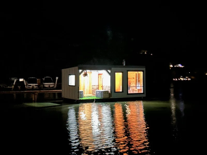 Floating sauna glowing at night with reflections on the water