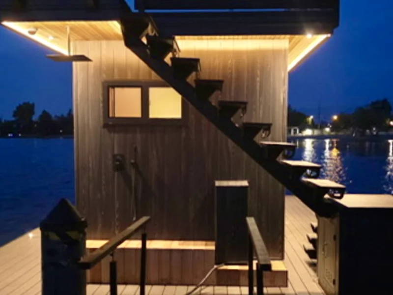 Night view of floating sauna with warm lighting and dock access