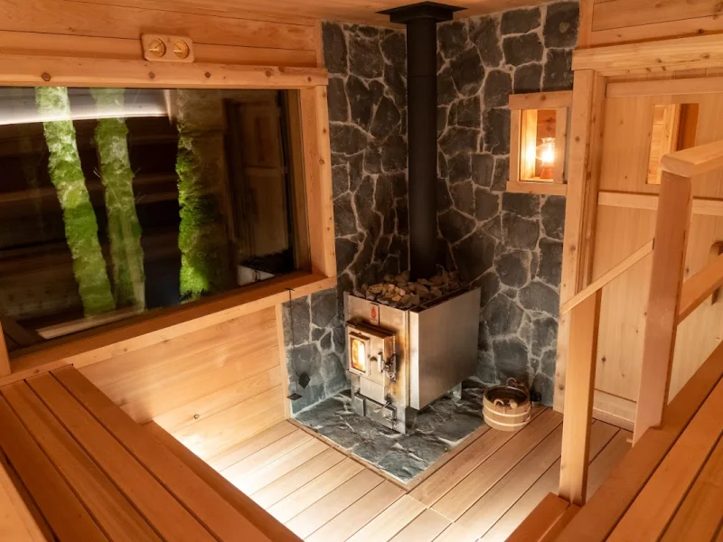 Cozy wood-fired sauna interior with stone heater and forest-view window