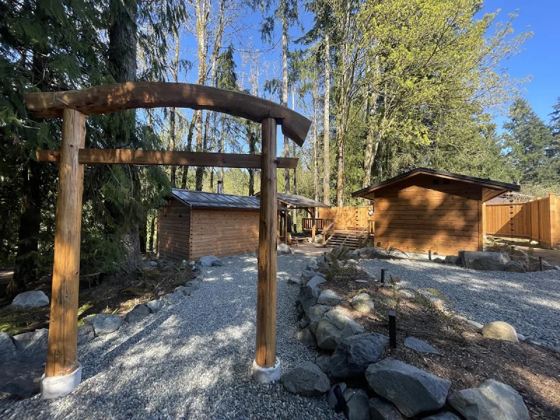 Wooded sauna retreat with gravel path, timber arch, and cabin exterior